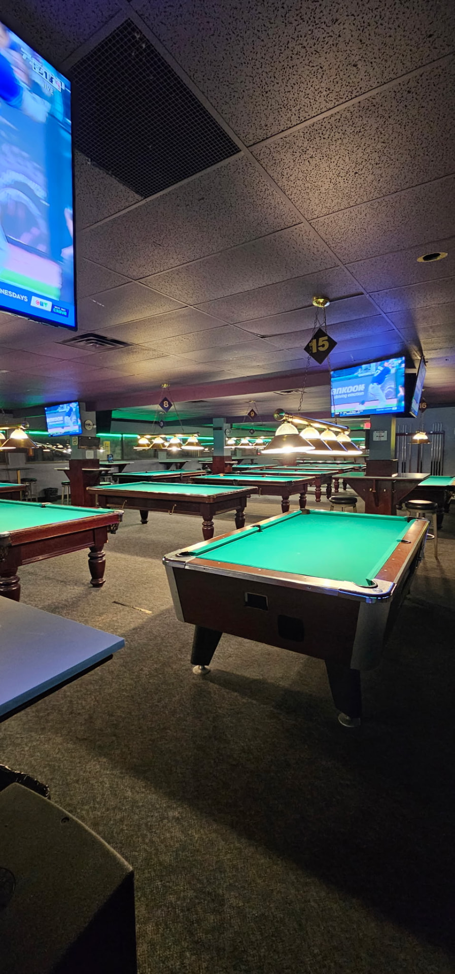 Green-felt pool tables and hanging lamps inside Boulevard Billiards