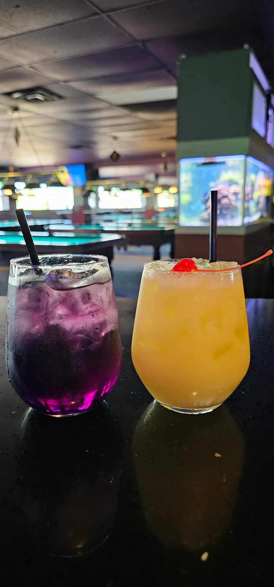 Two mixed cocktails on the bar with the pool tables behind them